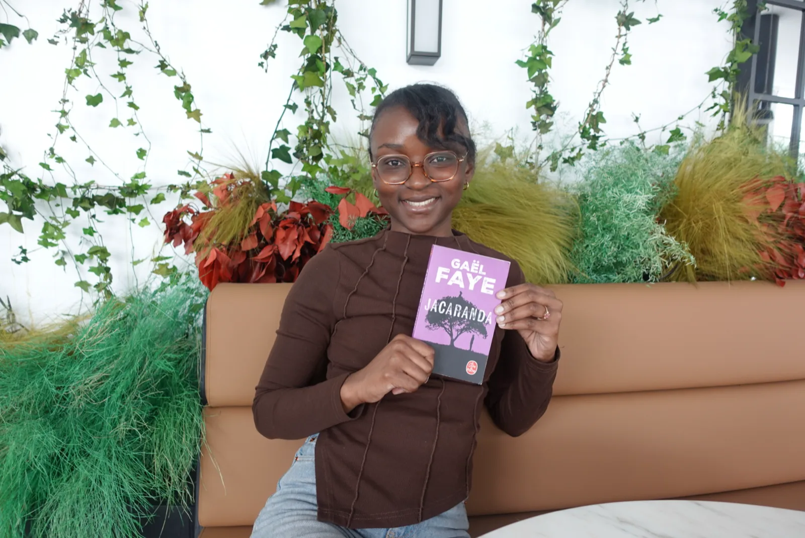 Divine souriante, tenant le roman Jacaranda de Gaël Faye